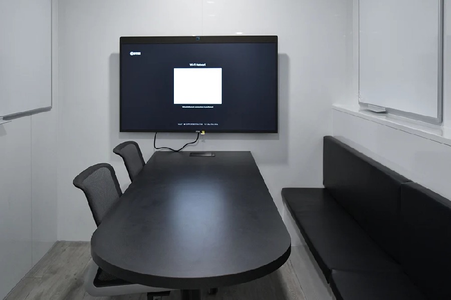 Interior conference room of a mobile command center, featuring a black oval table, black bench seating, a large wall-mounted monitor, and two mesh chairs.