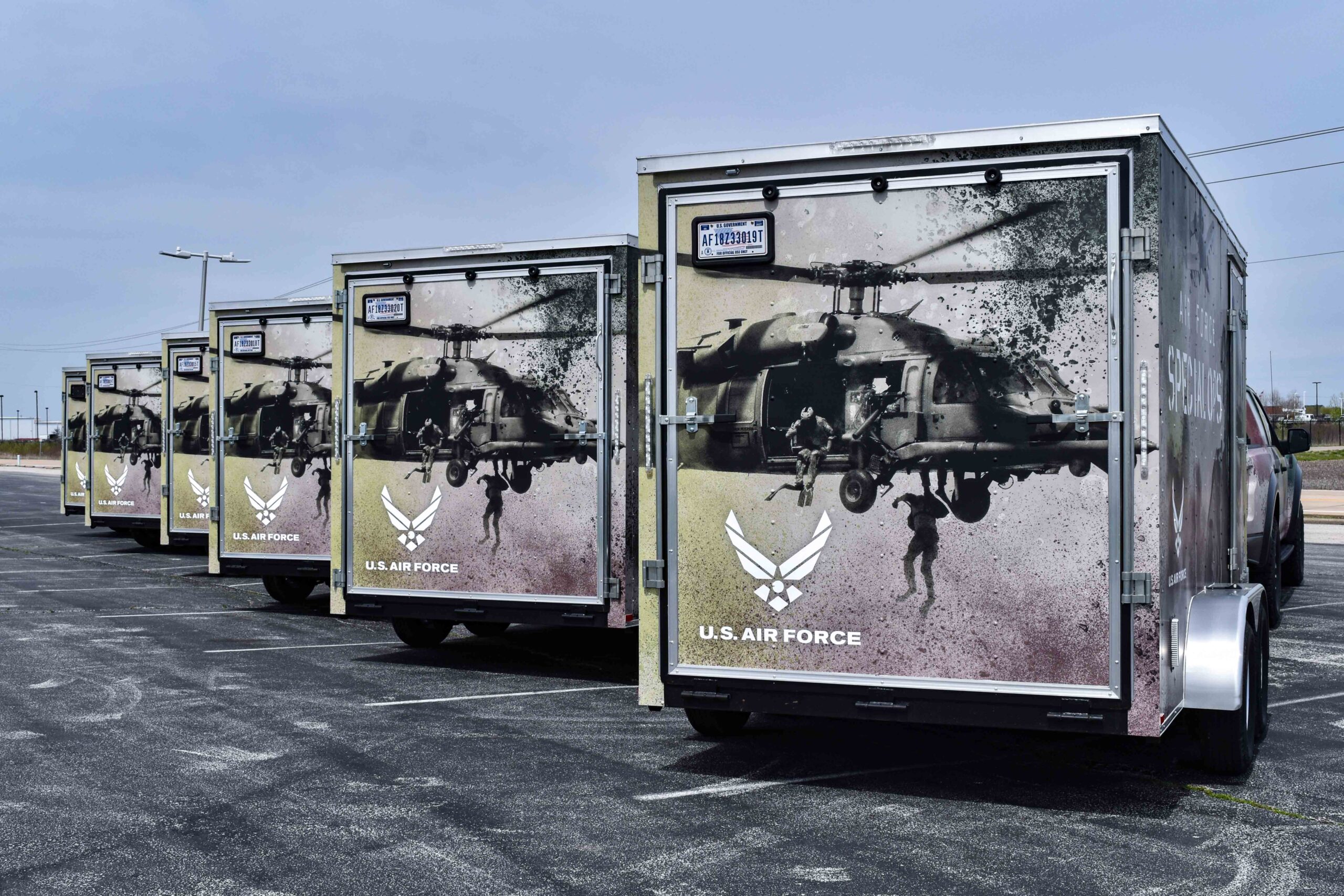 Row of four identical U.S. Air Force marketing trailers with powerful graphics of a Black Hawk helicopter and airmen rappelling, showcasing military-themed vehicle wraps.
