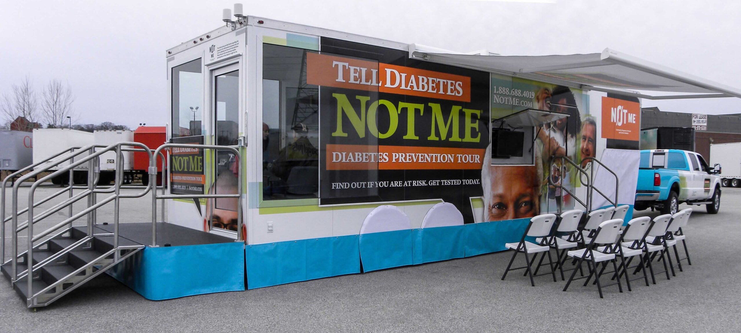 Tell Diabetes Not Me Diabetes Prevention Tour mobile trailer with large graphics, deployed stairs, an open awning, and a row of white folding chairs for an outdoor event.