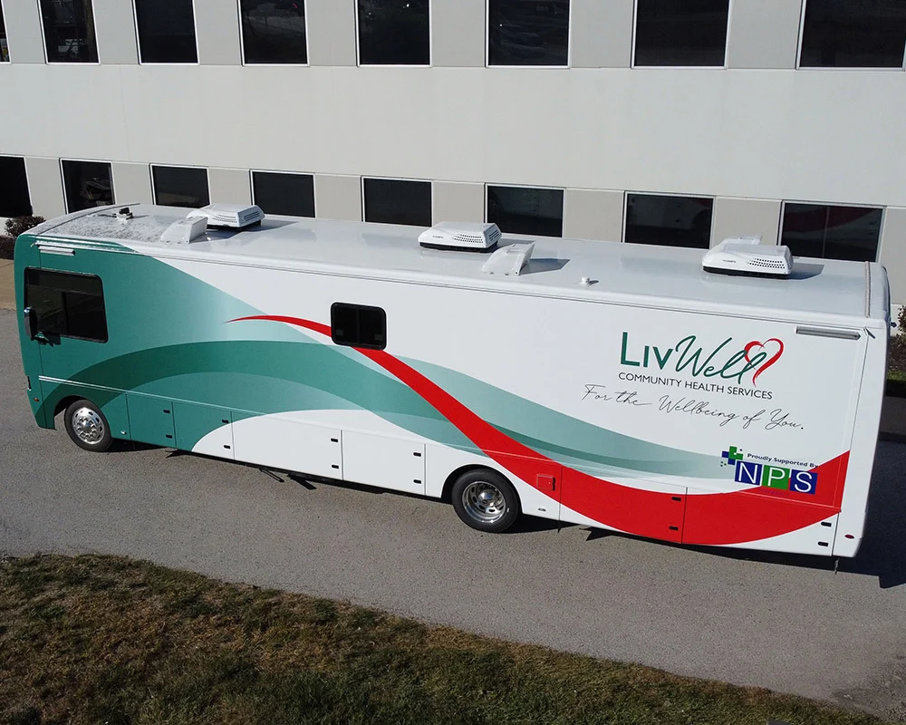 Overhead view of a custom-built LivWell Community Health Services mobile medical coach with green, white, and red branding, representing the typical manufacturing time and cost involved in building specialized medical vehicles.
