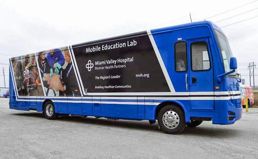 Miami Valley Hospital Mobile Education Lab coach, featuring blue and black branding and a graphic showing medical professionals training. This custom vehicle is an example of a full-size Medical Coach used for educational outreach.
