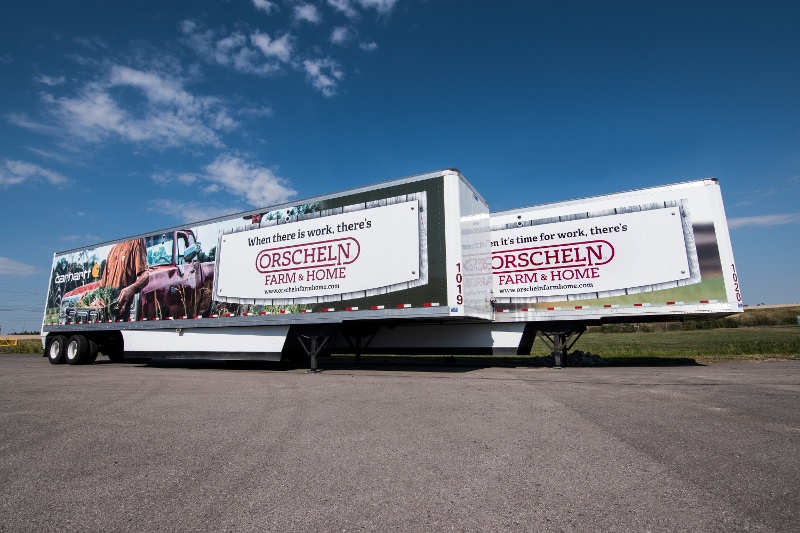 Orscheln Farm & Home double-expandable marketing trailer with large-format Carhartt and farm-themed fleet graphics, fully deployed in a parking lot under a blue sky.