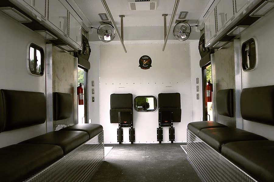Interior of the St. Louis Metropolitan Police mobile police station van, showing black fold-down benches and seats, fire extinguishers, and two interior fans mounted on the ceiling.