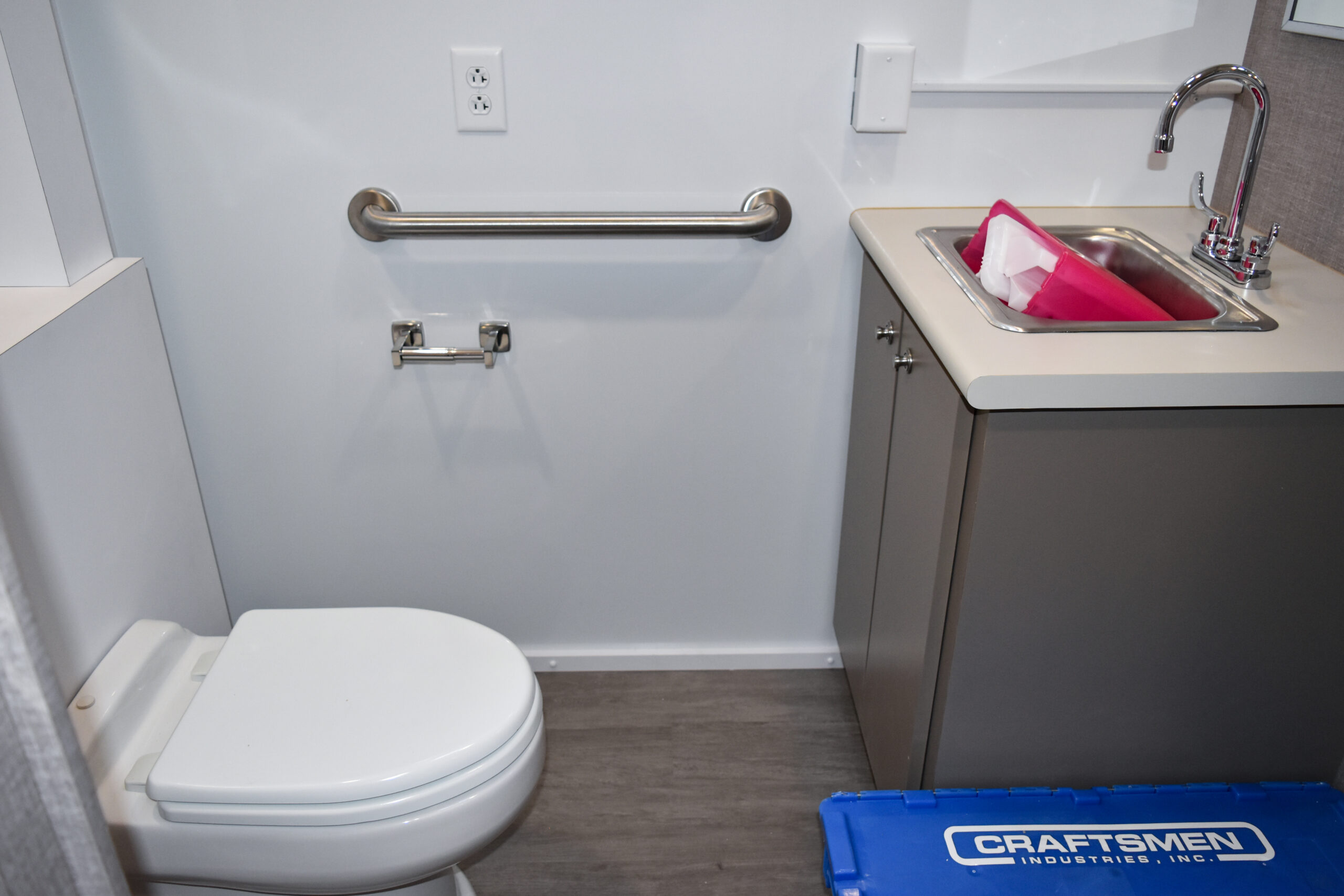 Interior of the Quest Diagnostic mobile medical vehicle restroom featuring a toilet, ADA-compliant grab bar, vanity sink, and under-sink storage cabinet. Designed for hygiene and patient accessibility.
