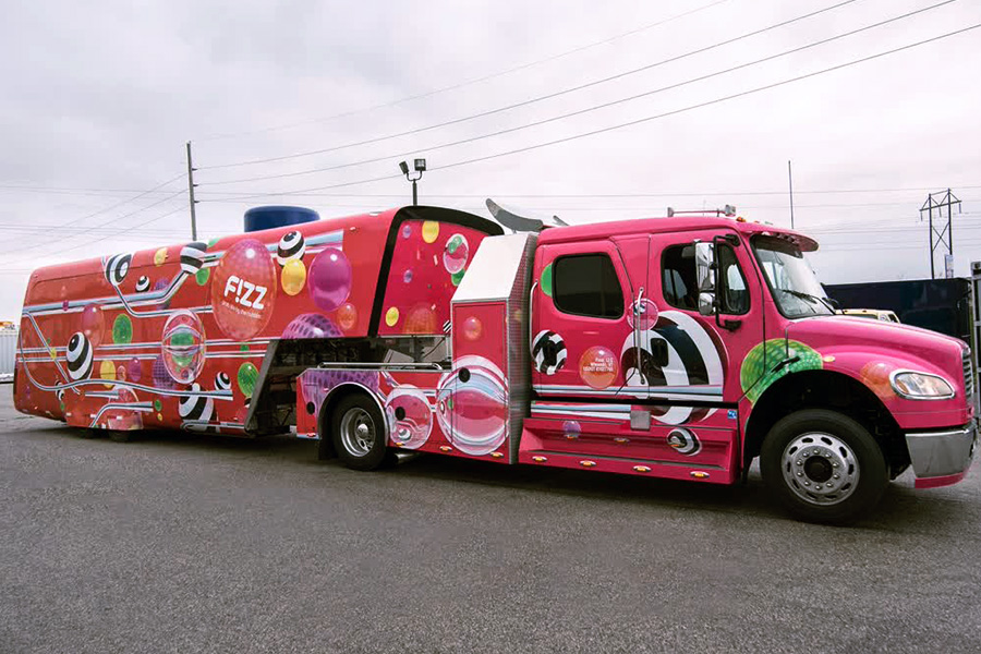 Large custom semi-truck and trailer wrapped in vibrant pink and red graphics with the "FIZZ" logo and bubble patterns, showcasing a highly stylized, eye-catching vehicle used for mobile experiential marketing events.