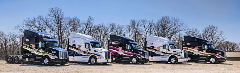 A fleet of five custom-wrapped semi-truck tractors from Wendy Boudreau Trucking, featuring alternating black and white cabs with striking red, gold, and pink graphic designs.