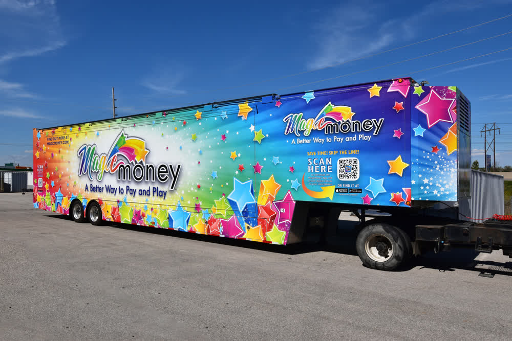 A large commercial trailer wrapped in a vibrant, multi-colored graphic. The design is covered in stars and sparkles and includes a prominent QR code to scan.