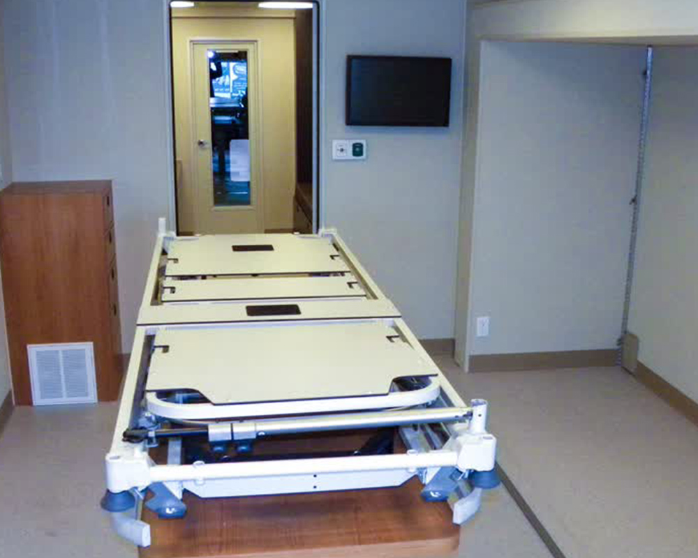 A white folding medical bed or stretcher, designed for easy storage and deployment, positioned within the interior space of a new or used mobile medical vehicle or trailer.