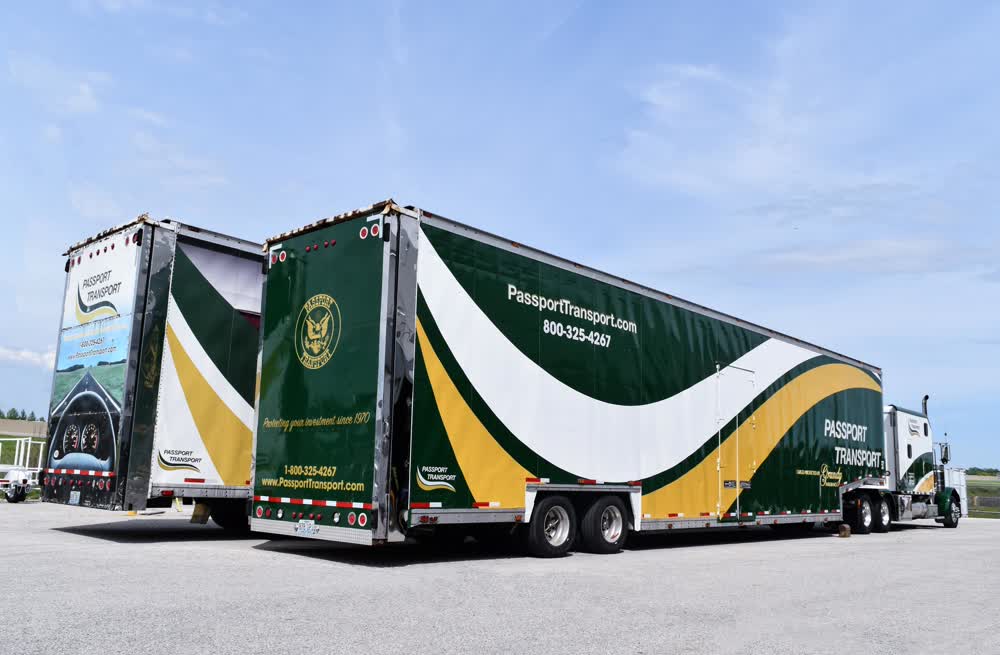 Two large Passport Transport semi-trailers with a distinctive dark green, white, and yellow custom graphic wrap and branding, parked side-by-side in an outdoor lot.