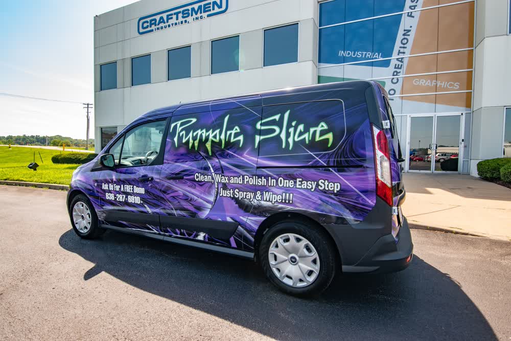 Side and rear view of a white van with a vibrant, high-gloss Purple Slice detailing product vehicle wrap, featuring a purple and black graphic design and product slogan, parked outside the Craftsmen Industries building.