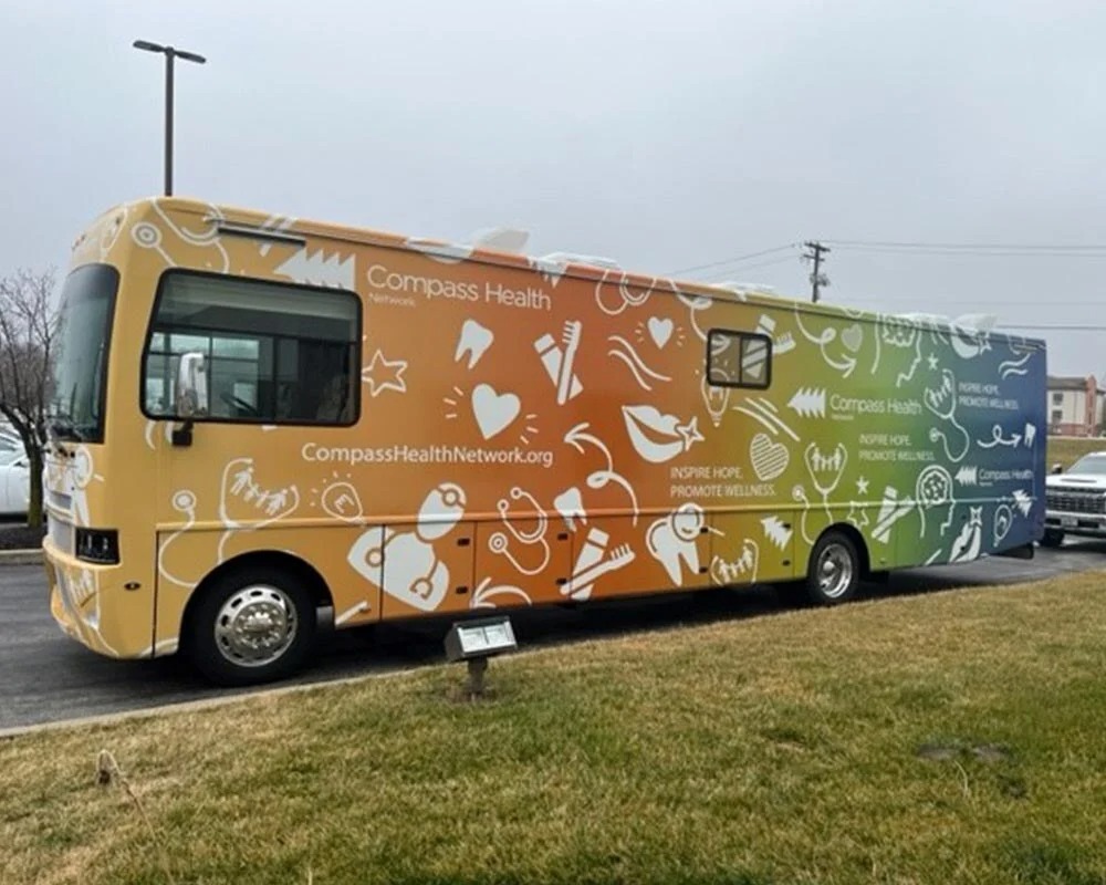 Compass Health mobile dental vehicle with a colorful, multi-colored graphic wrap featuring white icons representing dental, vision, and mental health services.