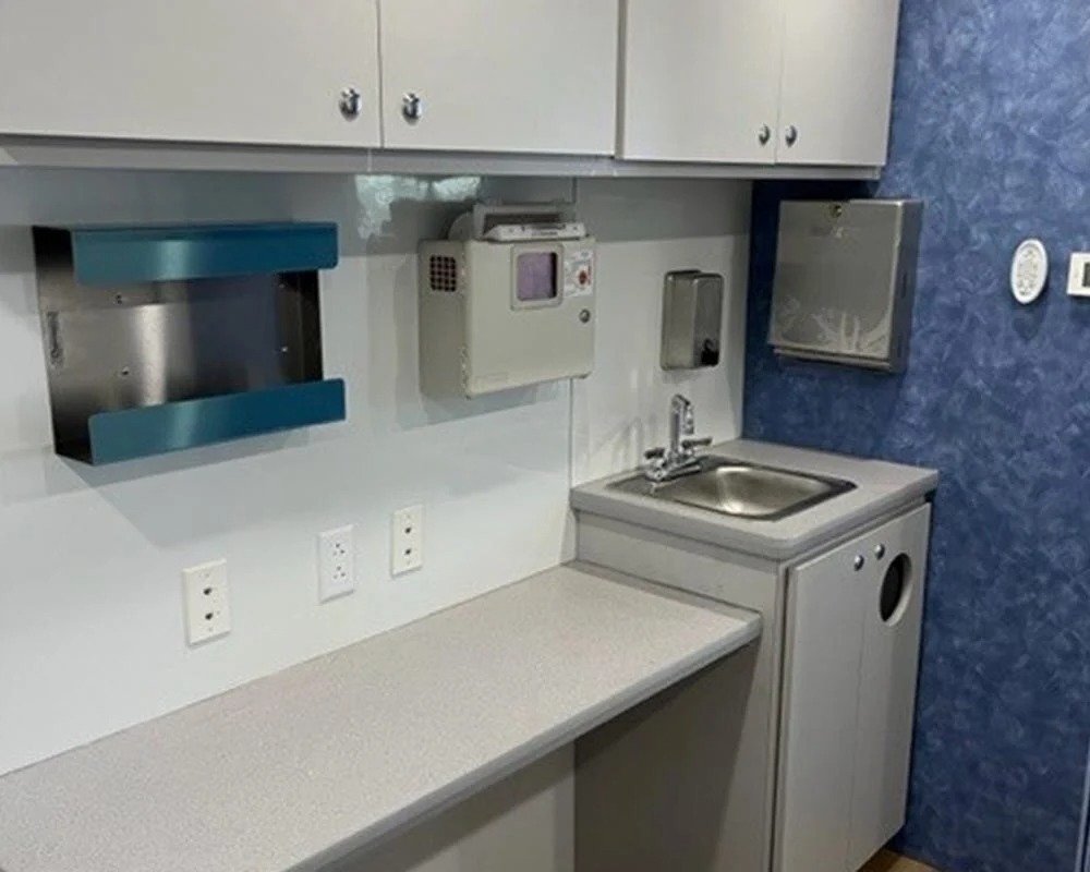 Interior of a mobile dental vehicle with a countertop, a sink, and drawers. The space features blue accent walls, white cabinets, and a desk area with a chair.