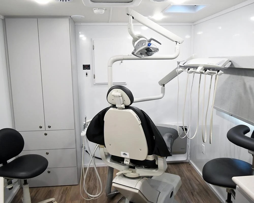 Interior of a Compass Health mobile dental clinic, featuring a dental chair, an adjustable overhead light, and a tray of dental tools.