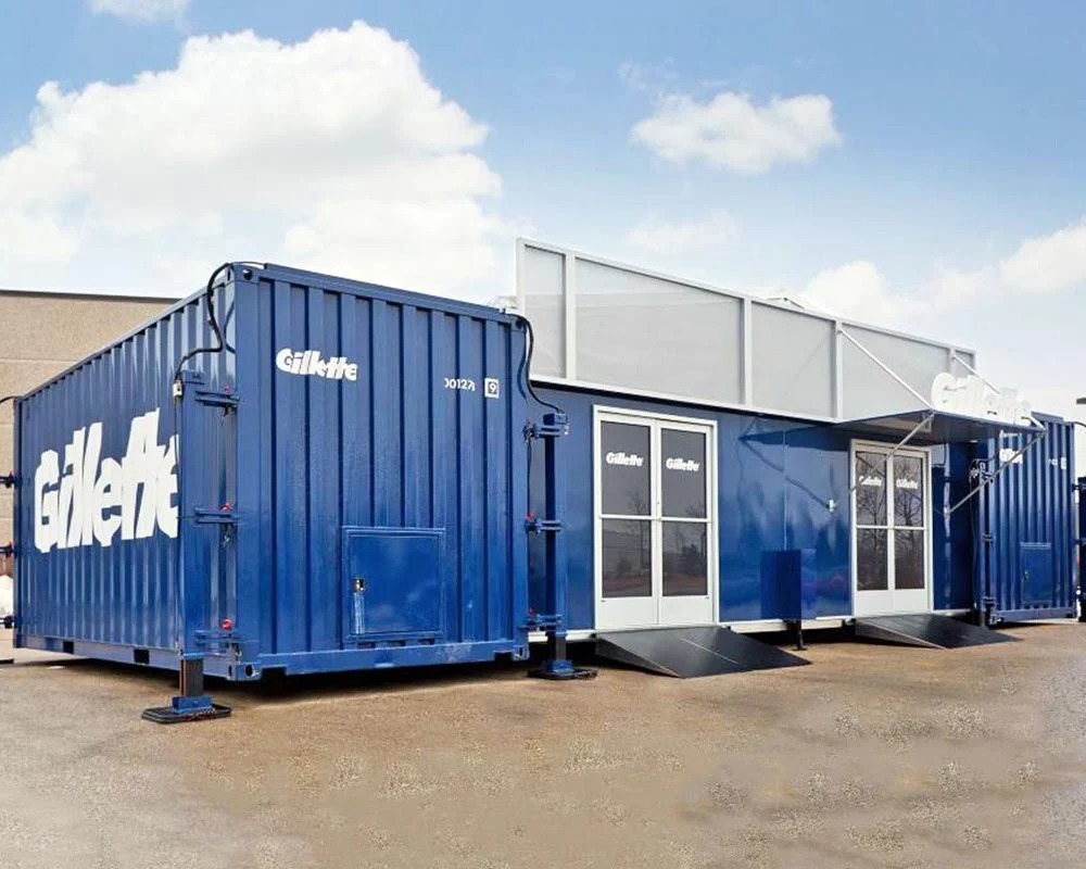 Large blue Gillette brand shipping container pop-up store with doors, ramps, and branding on the exterior.