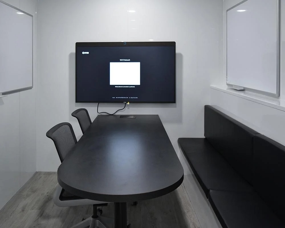 Interior view of a small mobile command center kitchen with a microwave, a refrigerator, a sink, and white cabinets.