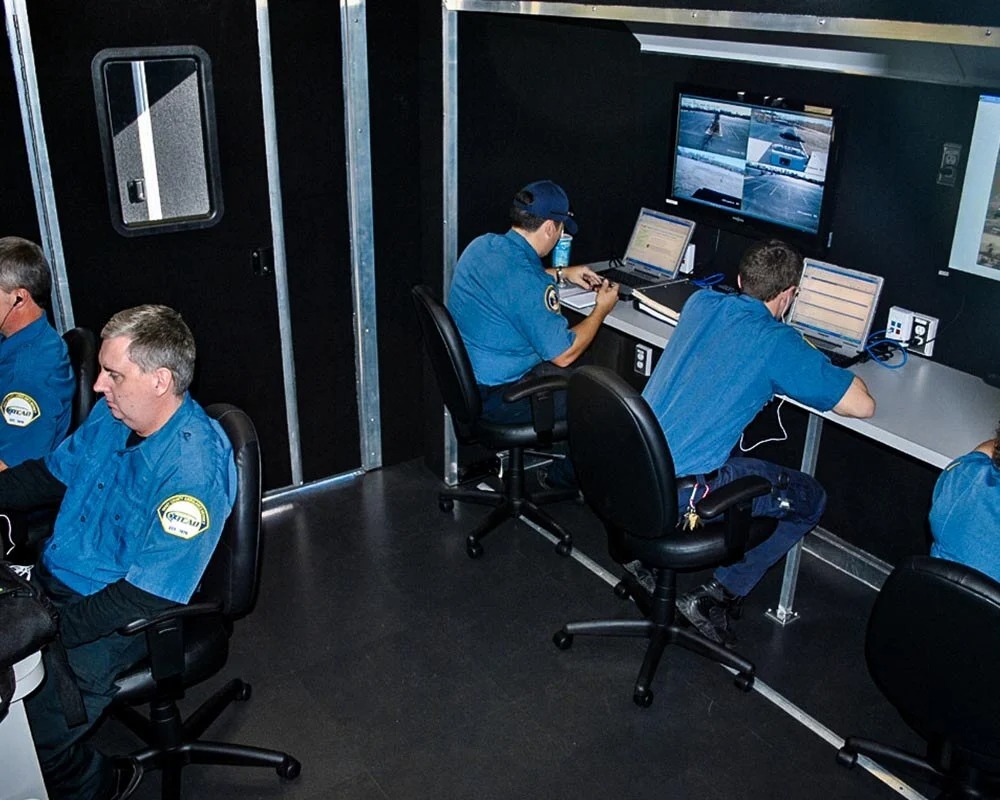 Interior view of the mobile disaster relief command center trailer with four men in blue shirts working at desks with laptops and a monitor.