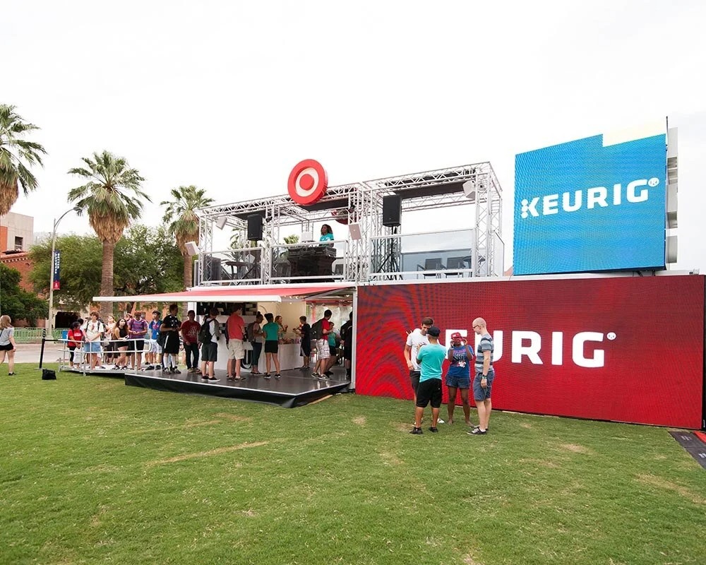 Target and Keurig shipping container conversion booth with a line of people on a grassy field