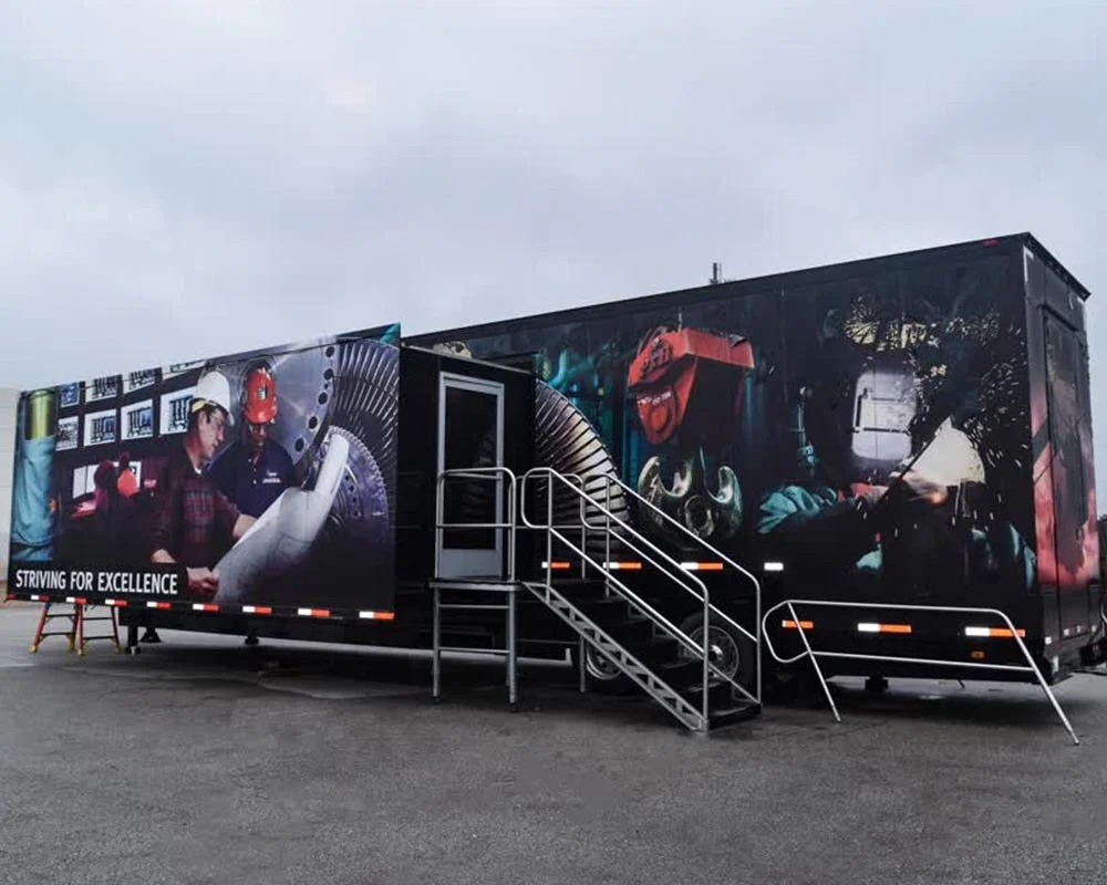 Exterior of a large, black Ameren training mobile command center trailer-2 unit wrapped with graphics of power plant workers and turbine machinery, featuring an entrance staircase.