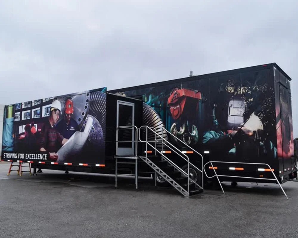 External view of a black Ameren training mobile command center trailer with an extended side panel featuring graphics of workers and a staircase leading to the entrance.