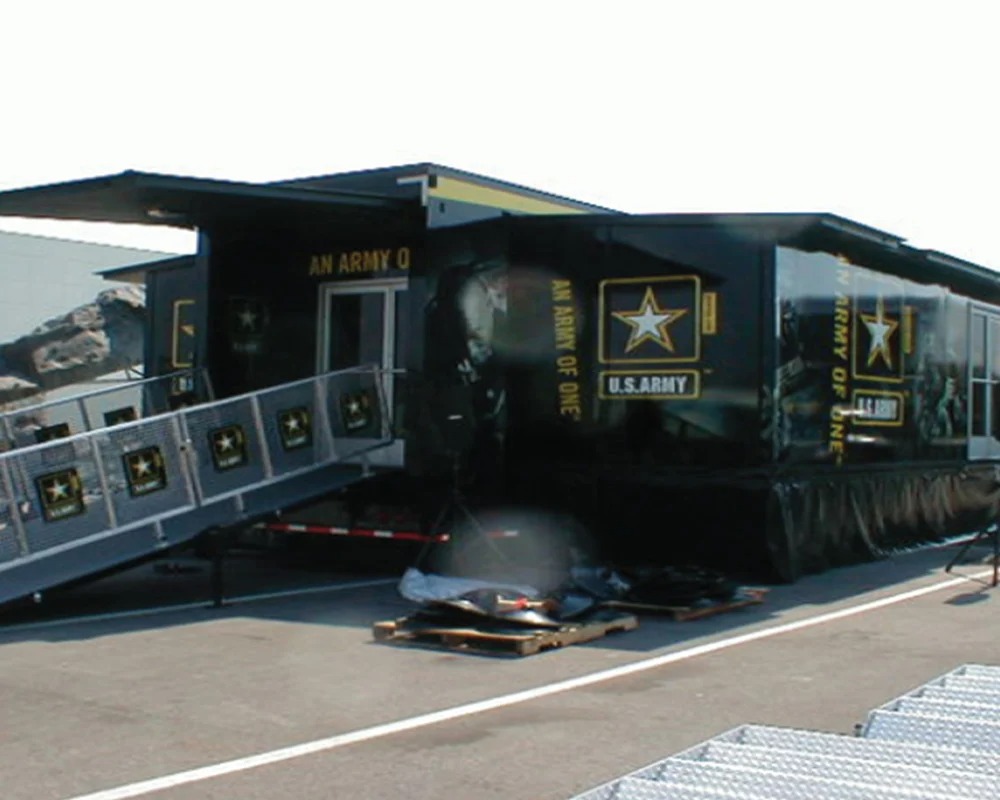 External view of a black U.S. Army mobile recruitment trailer with a large star logo, a side panel expanded, and a staircase with a handrail leading to the entrance.