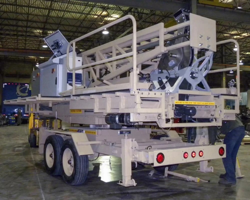 Rear view of a heavy-duty, tan industrial fabrication lift or mobile platform mounted on a multi-wheel trailer with stabilizer jacks.