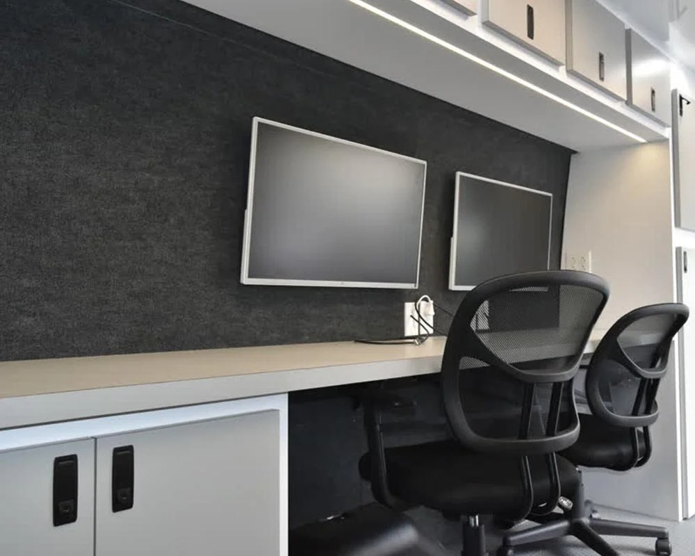 Inside a mobile police office showing a desk with two computer screens and two chairs