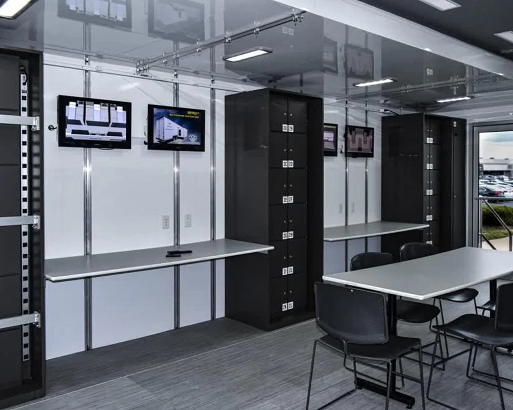 Interior view of a multipurpose mobile command center trailer with multiple mounted monitors, workstations, a conference table, and office chairs.
