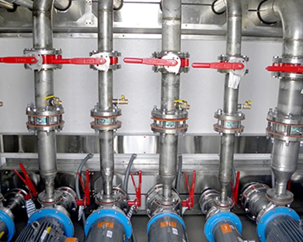 Close-up of vertical stainless steel pipes with red-handled valves and industrial water pumps at their base.