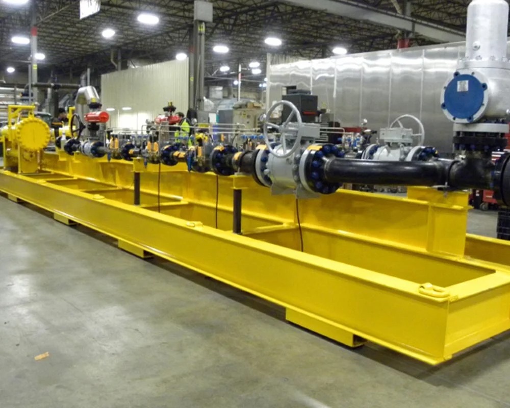 Long industrial fabrication skid with bright yellow steel frame supporting complex water or fluid processing pipelines and valves.