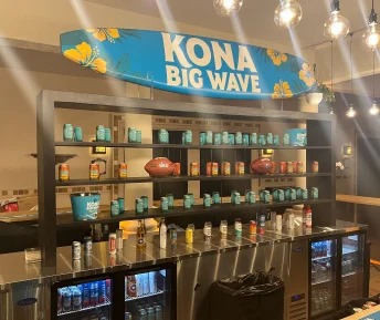 Kona Big Wave beer bar display with surfboard sign, product cans, and football props at Super Bowl event.