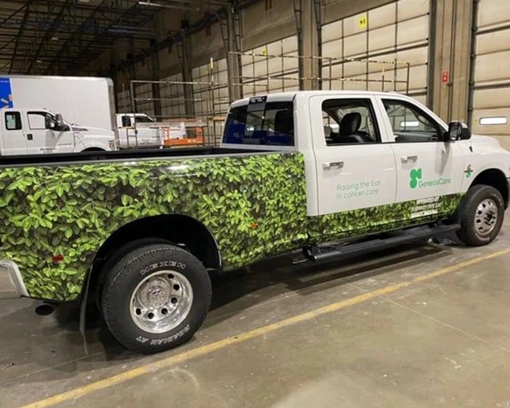 White GenesisCare pickup truck with a green leafy custom full-body vehicle wrap for cancer care advertising.