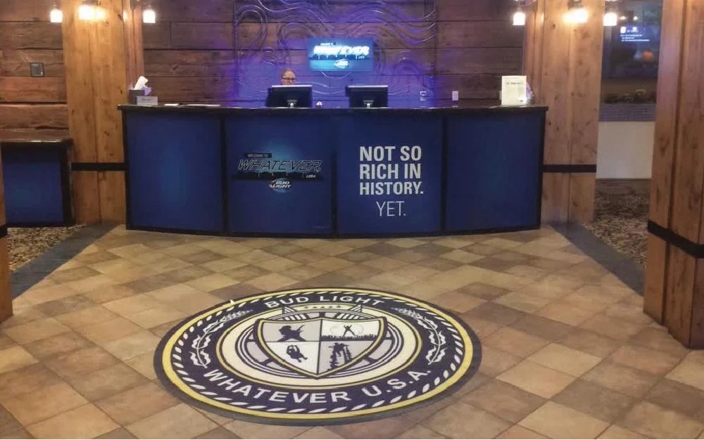 Bud Light Whatever USA floor graphic and branded reception desk inside a wood-paneled event or hospitality area.