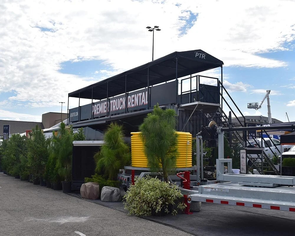 Premier Truck Rental (PTR) double-decker hospitality trailer with rooftop viewing deck and branded black awning.