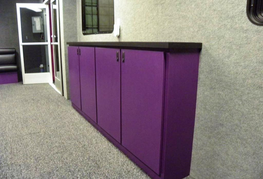 Interior view of a gym locker room or facility area, showing a long set of vibrant purple cabinets with black countertops and a gray carpeted floor, consistent with Planet Fitness branding