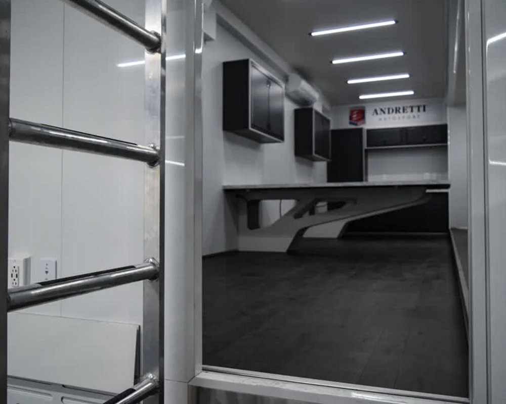 Andretti Autosport race car trailer interior view through doorway showing built in desk cabinets and work area