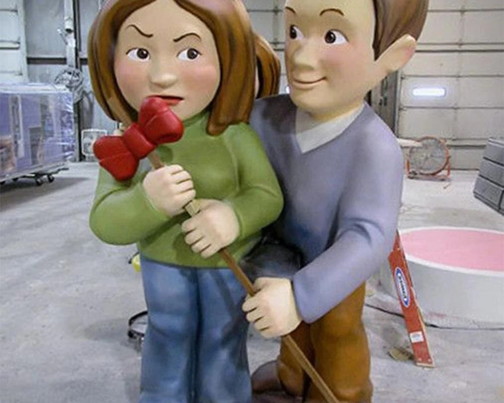 Giant cartoon character statues of a man and an angry woman holding a red bow prop for an Axe event.