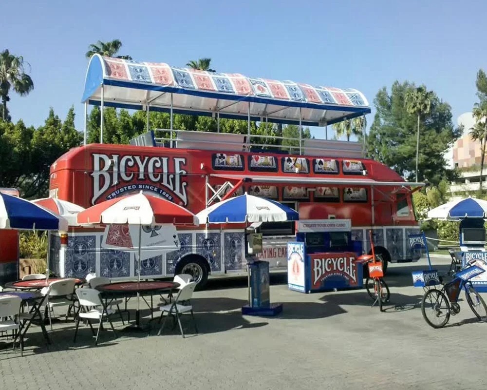 Bicycle Playing Cards promotional trailer at outdoor event featuring branded tables, umbrellas, and bikes for interactive marketing and customer engagement