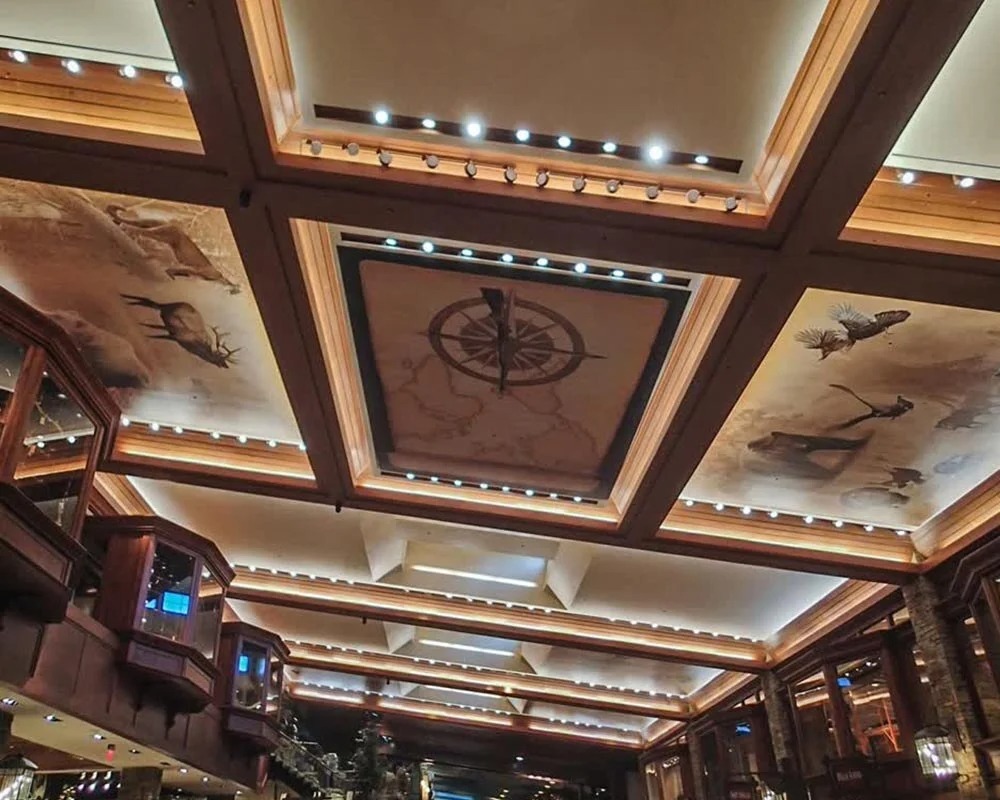 Lodge-style coffered wood ceiling with printed decorative canvas panels of a compass rose and wildlife illustrations.