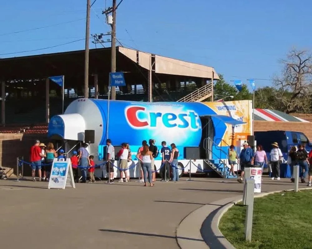 Crest promotional event trailer shaped like a toothpaste tube with people gathered around for a brand marketing activation outdoors.
