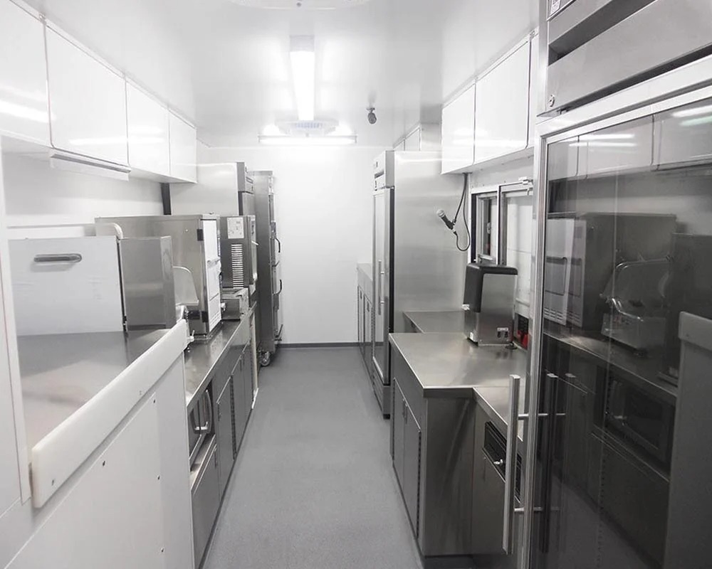 Bright, clean stainless steel kitchen interior of a custom food truck built by professional food truck builders, featuring commercial appliances and counters.