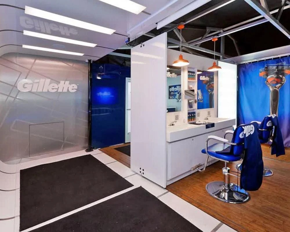 Gillette interior shipping container conversion into a modern shaving salon/showroom with white fixtures, blue chairs, and wood flooring for product activation.
