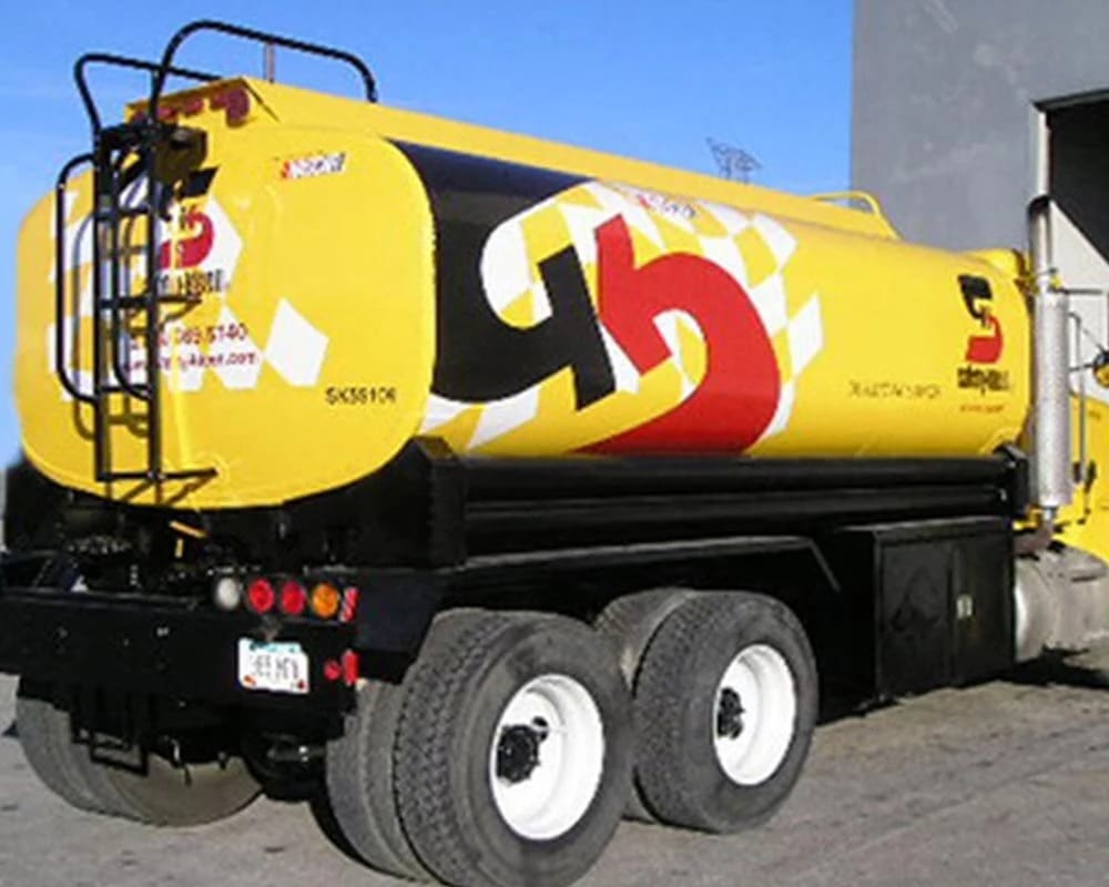 Rear three-quarter view of a bright yellow commercial tanker truck with bold black and red graphics of the number '5' and a checkerboard pattern, featuring the NASCAR logo and 'Citgo' branding, mounted on a black chassis with dual rear axles.