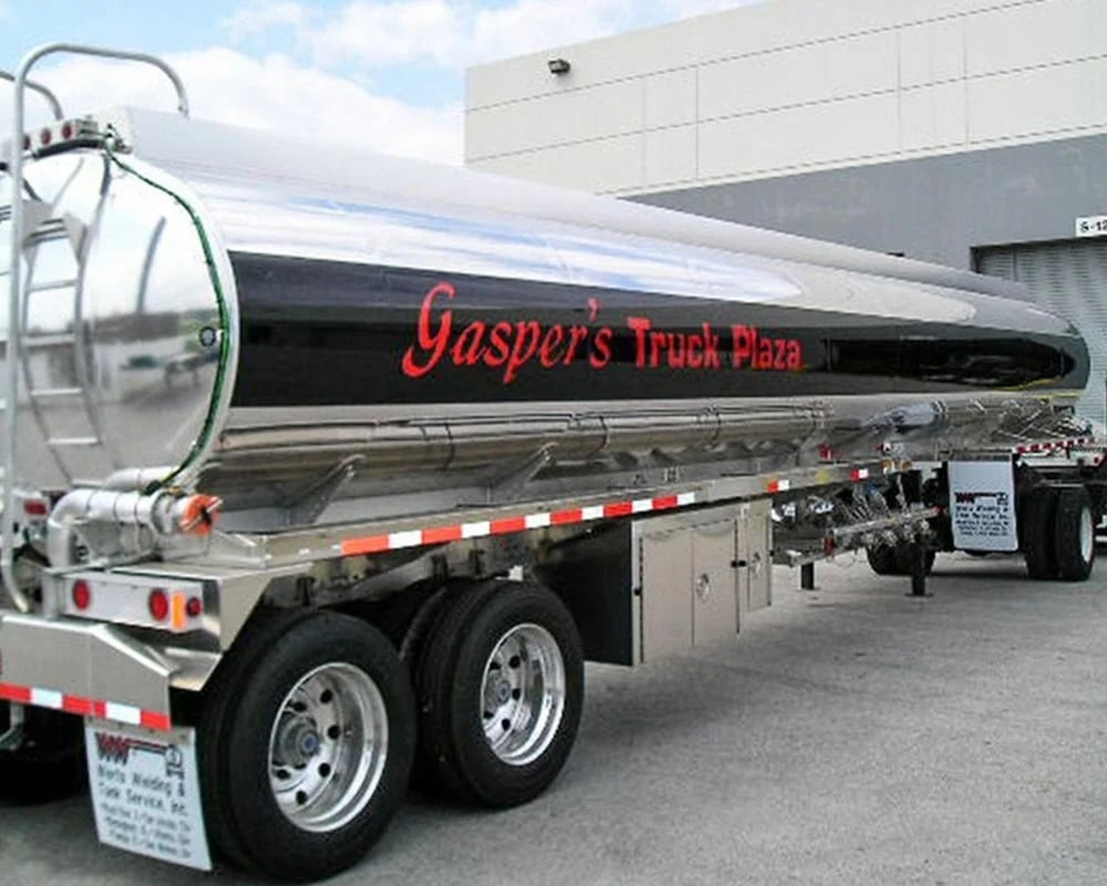 Close-up of a highly polished stainless steel commercial fuel or liquid tanker trailer, featuring a black central band with