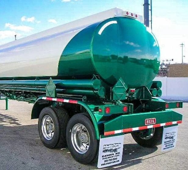 Close-up of the rear of a specialized tanker trailer, featuring a large white and bright emerald green tank, tandem axles with chrome wheels, a