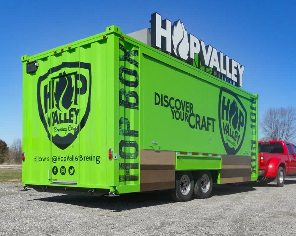 Bright green Hop Valley Brewing Co. mobile billboard trailer with a large rooftop sign and