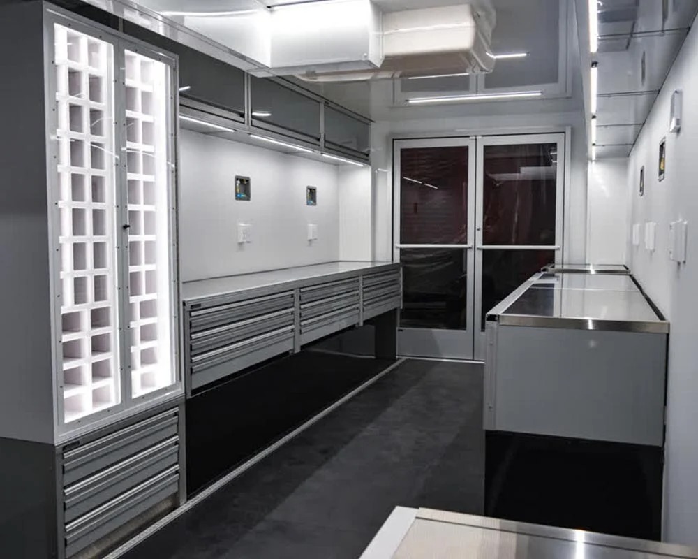 Interior view of a professional race car trailer showing cabinets drawers lighting and workspace