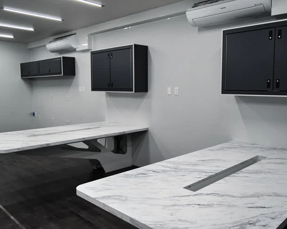 Interior of race car trailer showing two large marble look work tables black cabinets and air conditioning units