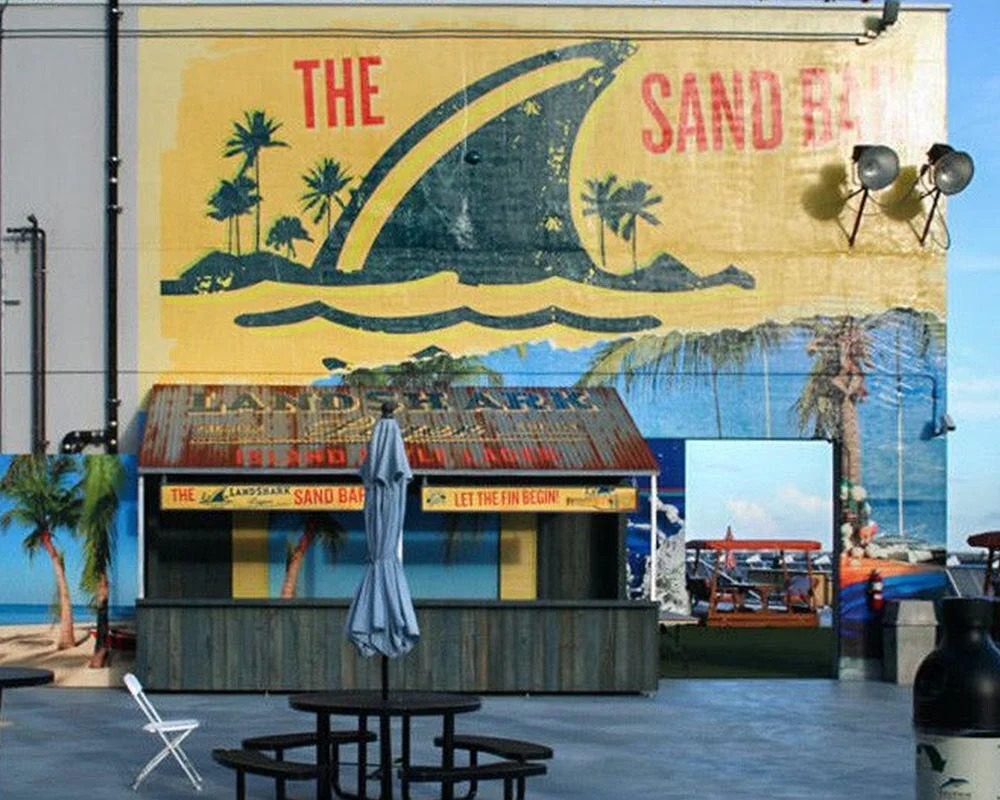 Outdoor stadium rooftop bar called The Sandbar, with a mural featuring a giant shark fin, palm trees, and the Landshark brand logo.