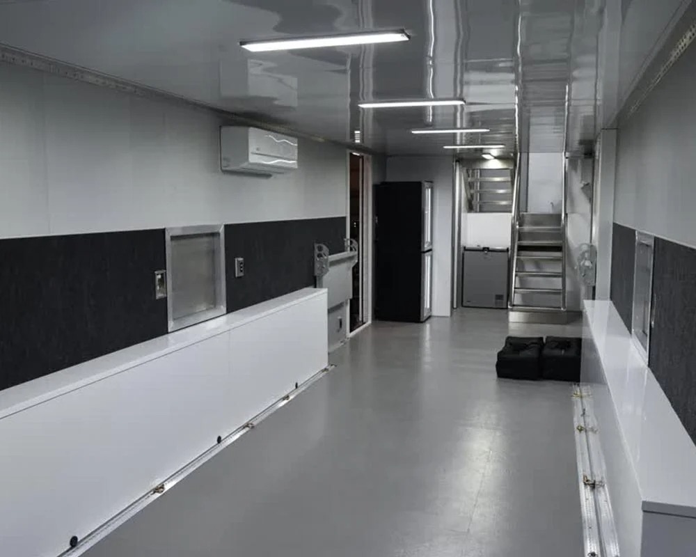 Marco Polo Motorsports interior motorcycle trailer lounge area with white lower cabinets, black upper cabinets, refrigerator, and a staircase to the second floor.