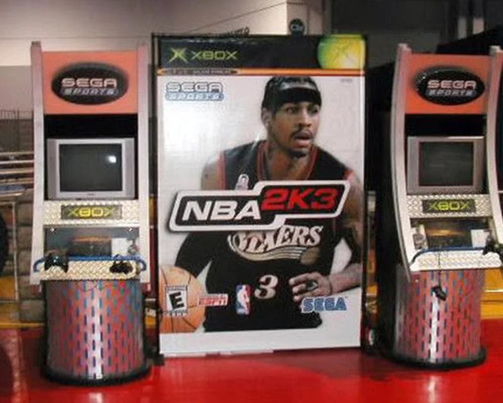NBA 2K3 video game display with giant Allen Iverson cover art between two Sega Sports Xbox arcade cabinets.
